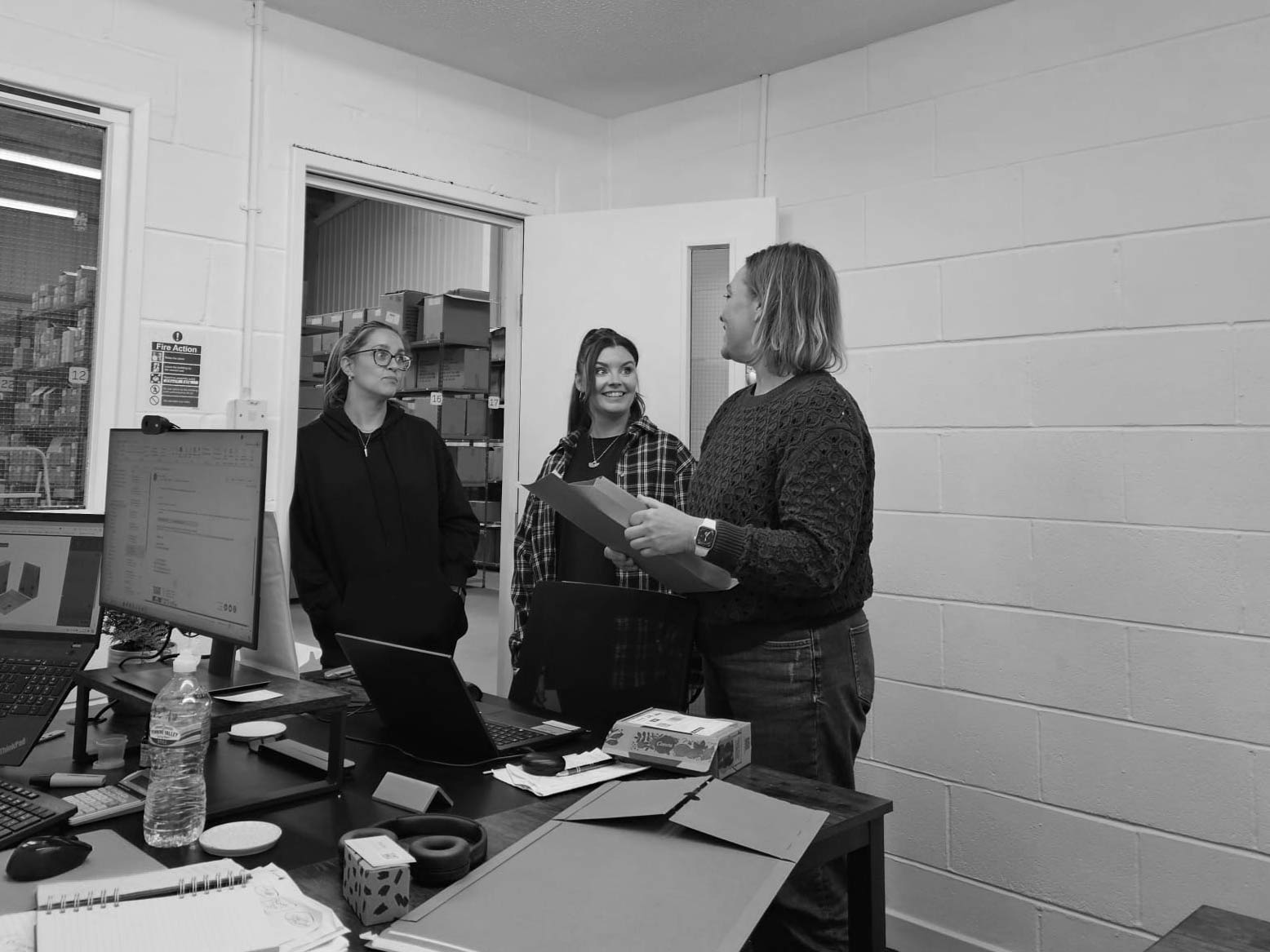 Three people in a room with desks and computers