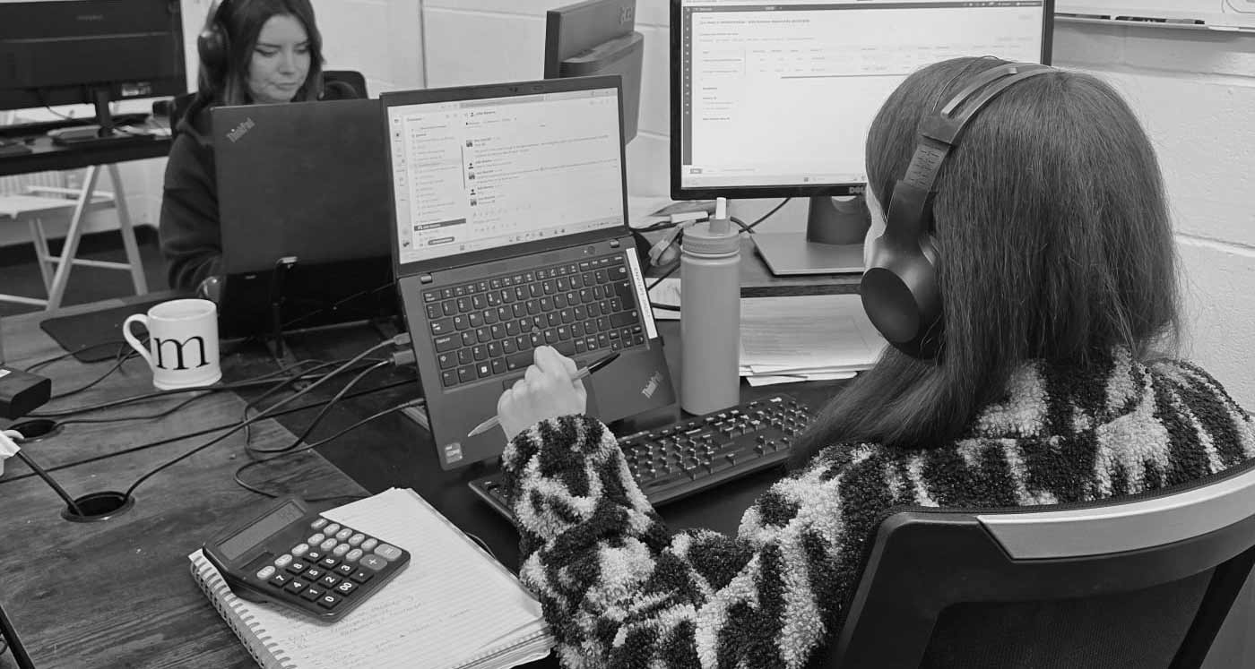 Person working at a desk with multiple computer monitors and a small dog on their lap.