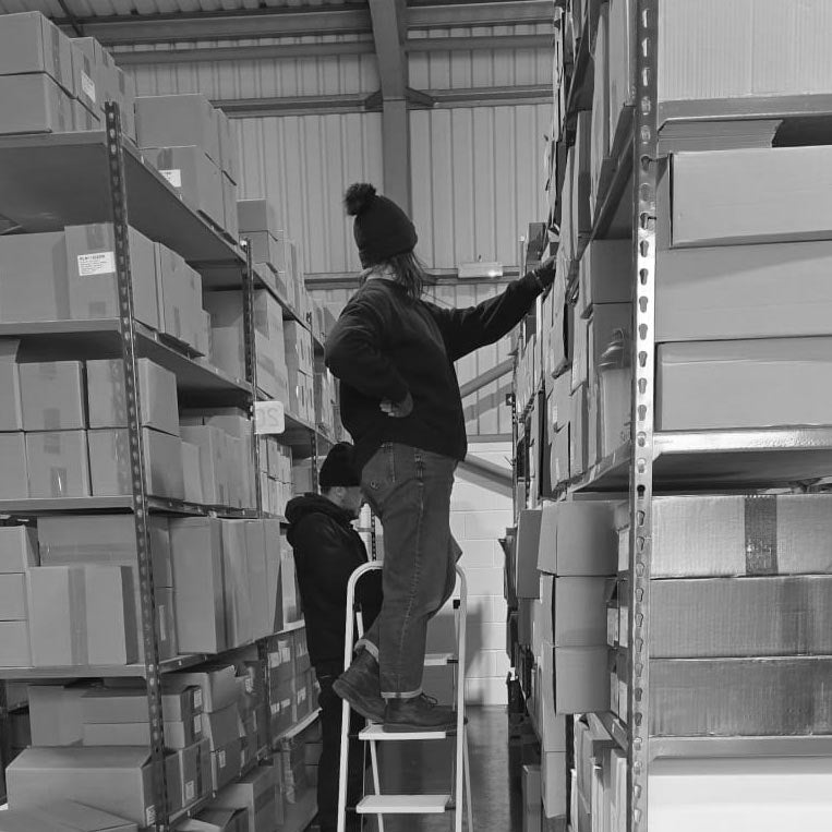 Two people working with shelves filled with boxes in a warehouse.