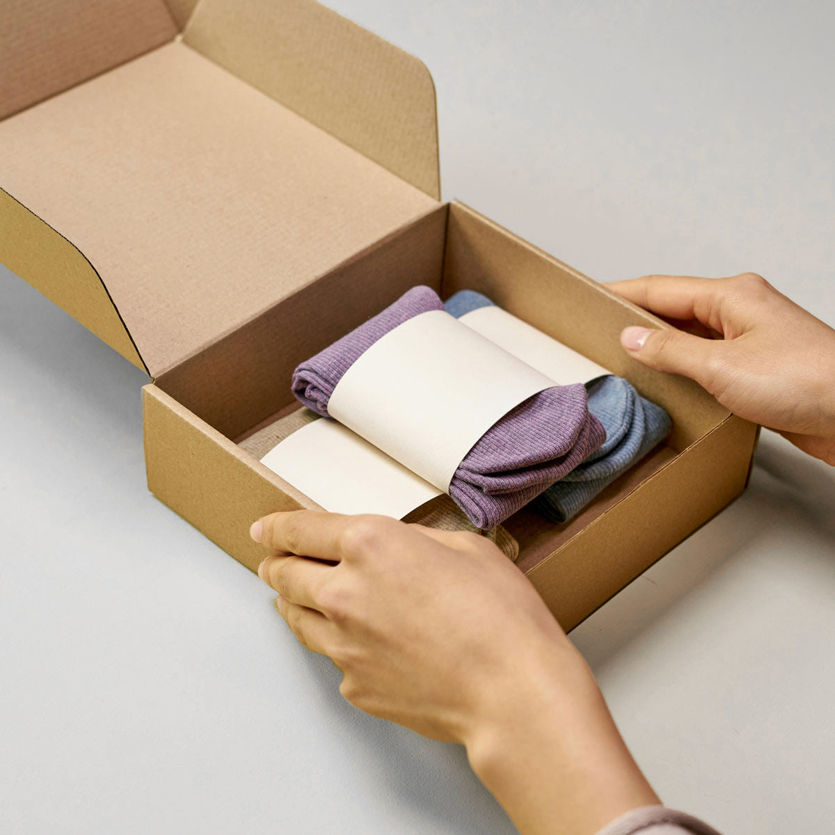 Person opening a cardboard box containing folded socks in various colors.