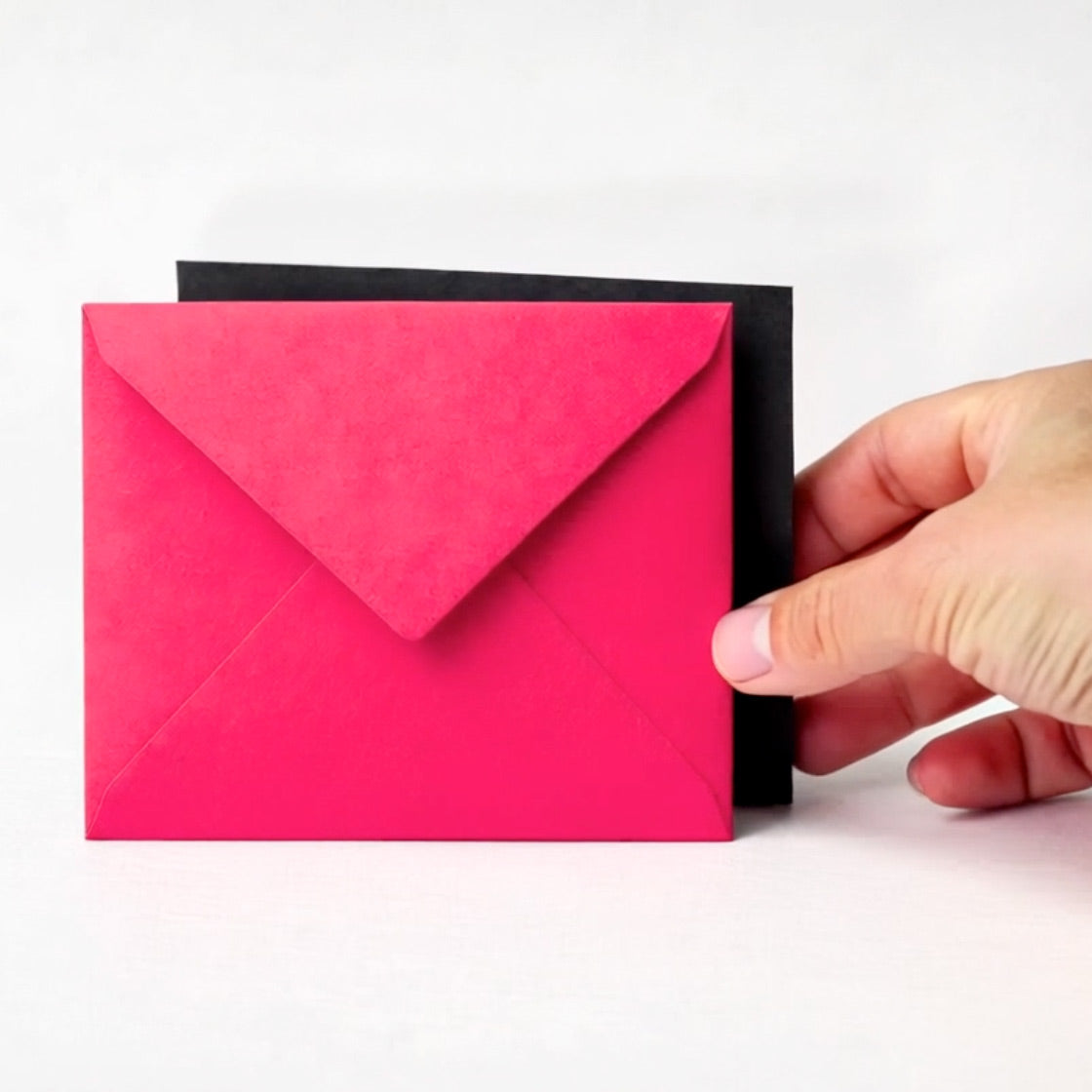 Hand holding a pink envelope against a white background