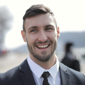 Man in a suit smiling outdoors with a blurred background