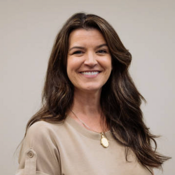 Woman with long brown hair wearing a beige top against a plain background