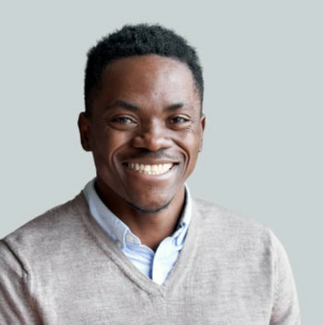 Man wearing a light gray sweater over a collared shirt on a plain background